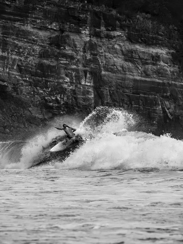 A surfer carving a closing wave below a dark cliff, El Zonte, El Salvador