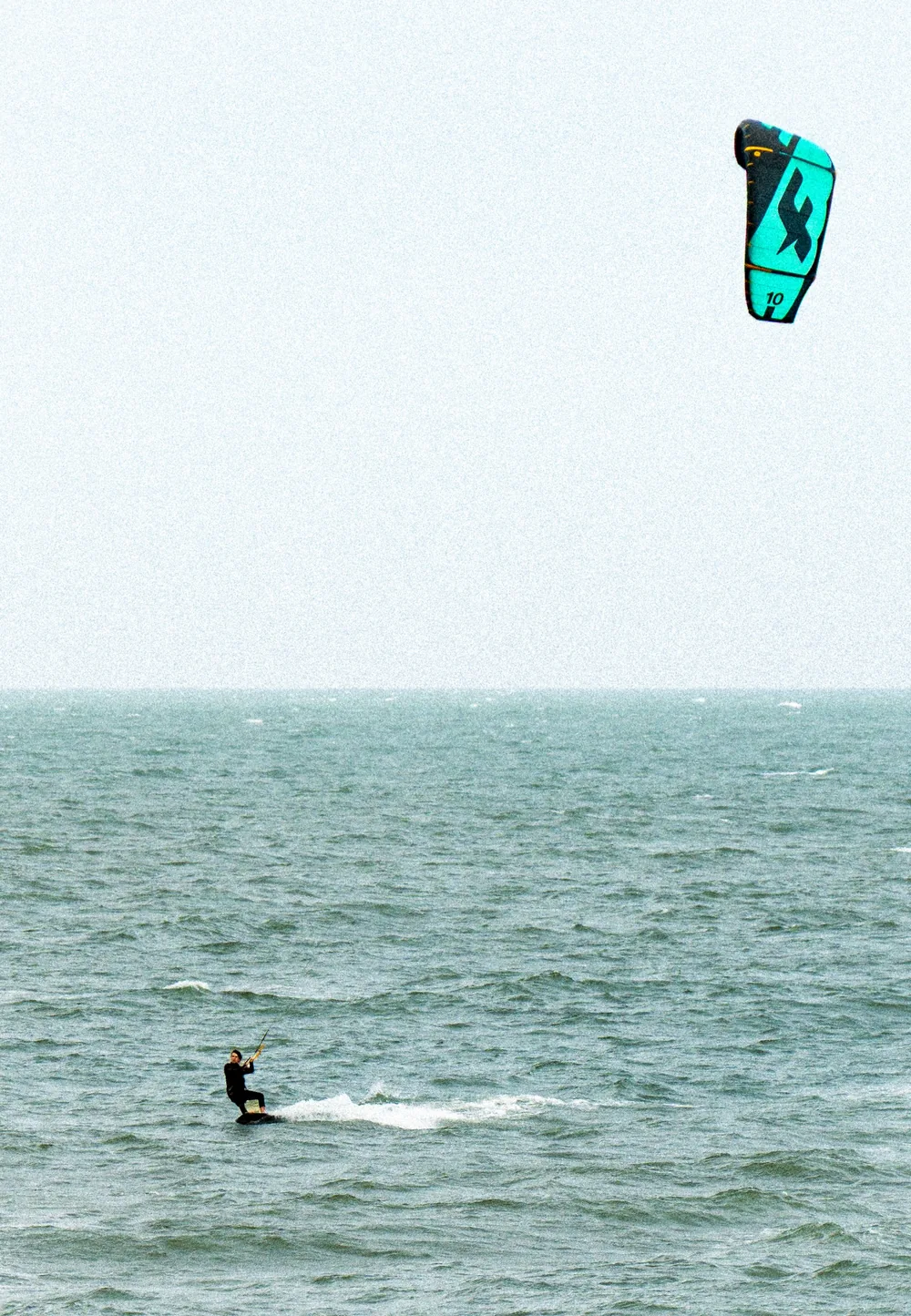 A kitesurfer on grey-green water, the kite high in a pale sky, Punta del Este, Uruguay